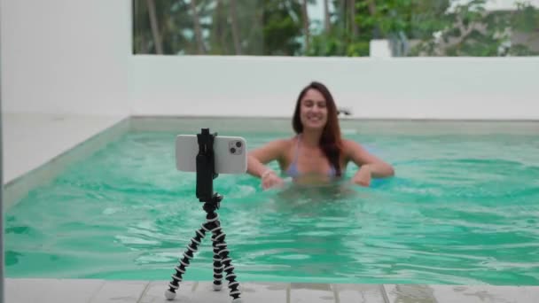 Joven blogger grabar en la cámara para contenido de redes sociales utilizando el teléfono en el trípode al aire libre, de cerca. Ella disfrutando en la piscina. — Vídeo de stock