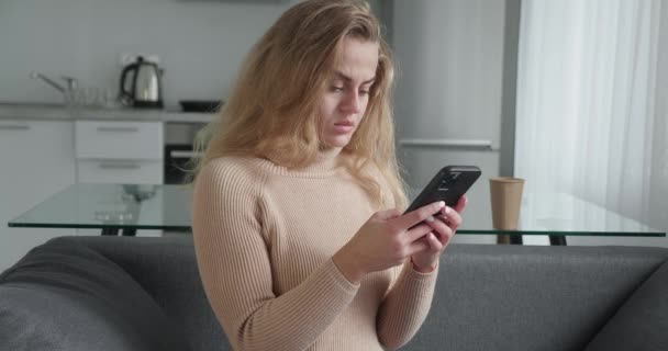 Zasněný pozitivní krásná mladá dívka v ležérní oblečení sedí gauč doma, když přemýšlí o odpovědi při chatování s přáteli na sociálních sítích — Stock video