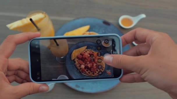 Женщины руки с помощью смартфона, чтобы сфотографировать вафли с красными фруктами и манго — стоковое видео