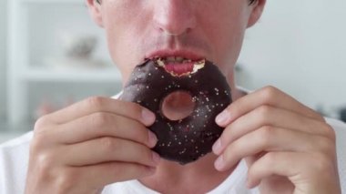 Beyaz arka planda çikolatalı donut yiyen bir adam..