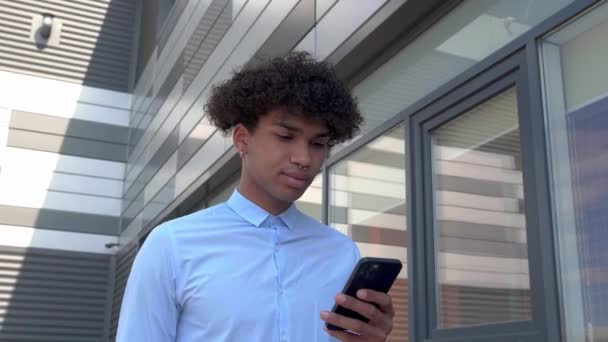 Een man in een shirt loopt door de zakenwijk en kijkt in een smartphone. Schieten in beweging — Stockvideo