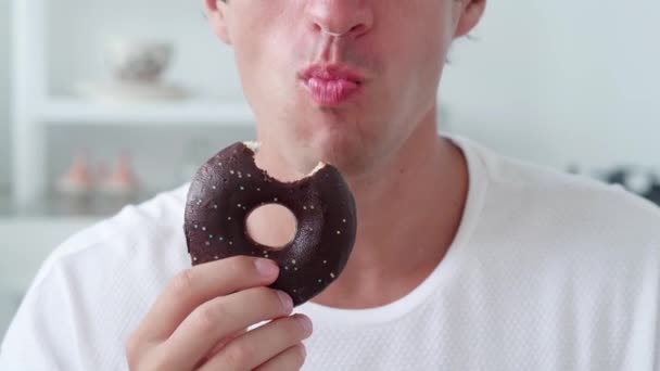 Homem comendo um donut em esmalte de chocolate com polvilhas. Close-up — Vídeo de Stock