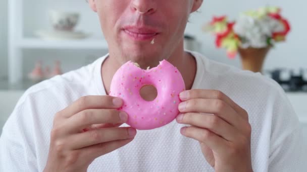 Homem comendo um doce donut em esmalte rosa com polvilhas. Close-up — Vídeo de Stock