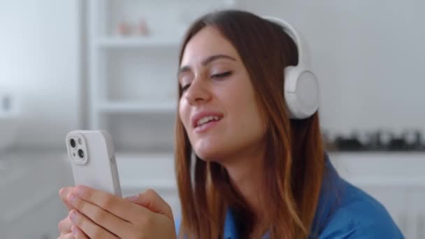 Close up kvinde i hovedtelefoner lytter musik i køkkenet baggrund – Stock-video