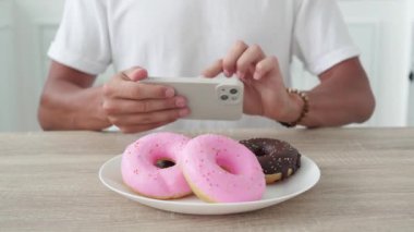 Tanımlanamayan bir adam akıllı telefondan donut fotoğrafı çekiyor.