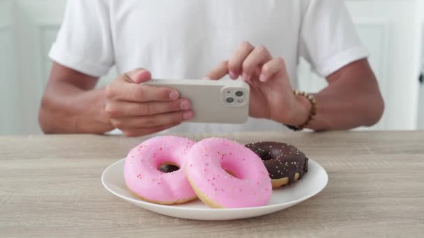 Tanımlanamayan bir adam akıllı telefondan donut fotoğrafı çekiyor. — Stok video