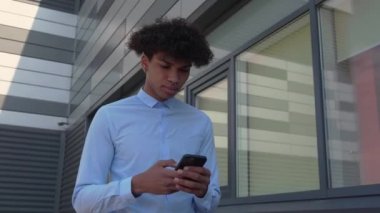 İyi giyimli bir iş adamı akıllı telefonuyla binanın yanında yürüyor.