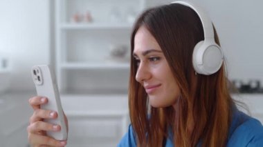 Akıllı telefondan haberlerde sörf yapan ve en sevdiği şarkıları kablosuz kulaklıkla dinleyen hoş bir kız.