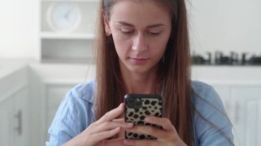 Woman resting in kitchen lean at dining table hold smartphone choose goods on internet, make food delivery order on-line. Modern wireless tech simplifies life, easy e services usage concept