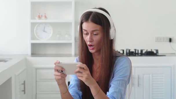 Piękna Dziewczyna Siedzi Kuchni Kobieta Słuchawkach Relaks Gra Jej Smartfona — Wideo stockowe