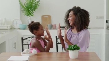 Mom and daughter clapping hands, having fun, enjoying time together in cozy light home kitchen interior. Togetherness.