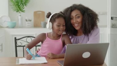 Multiethnic little girl drawing with felt-tip pens while browsing online drawing lesson on digital gadget