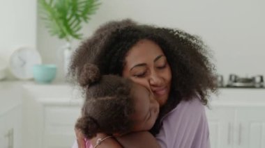 Close-up portrait of a happy African young woman, loving mom hugging her adorable elementary age daughter. Mothers Day
