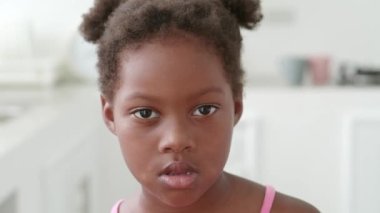 Headshot of a charming serene African preschooler girl, confidently looking at the camera at home kitchen background