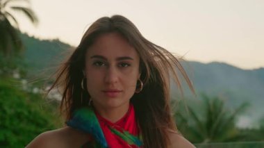Close up portrait of beautiful young woman with brunette hair blowing in the wind at mountain background.