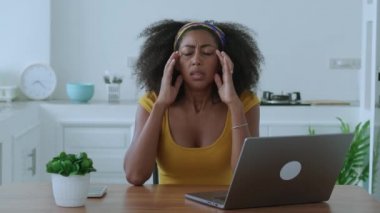 Multitasking woman suffers from migraine, massaging her temples for calm the pain due to computer stress after hard work