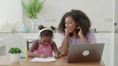 Experienced African woman, tutor is engaged in lessons at home with a preschooler child girl, explaining drawing courses