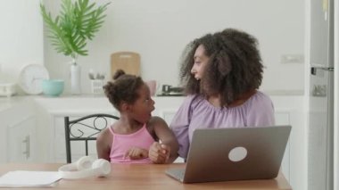 Cheerful woman and little girl watching movie on laptop, expressing surprise, smiling together looking at each other.