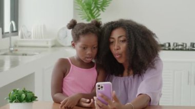 Mom and daughter sitting close to each other watching cartoons on smartphone, expressing surprise emotion from watched.