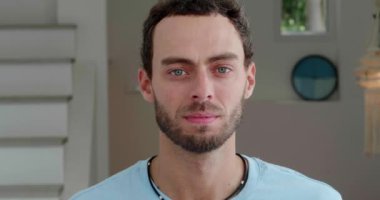 Close-up handsome Caucasian young man in casual wear, standing at home interior and confidently looking at camera.