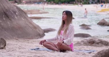 Young asian woman sitting and meditating on the beach with ocean background.