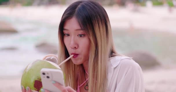 アジアの女性の手は スマートフォンのデジタルガジェットにサーフィンニュースを再生し 新鮮なココナッツを飲みます — ストック動画