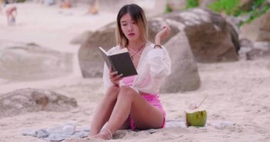 Asian woman relaxing, sunbathing, reading, drinking coconut water On the beach on vacation. concept of freedom, travel, adventure.