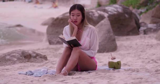 穿着比基尼的年轻美丽的亚洲女人是一个休闲的 日光浴的 阅读的 度假时在海滩上喝椰子水的女人 概念自由 生活方式 — 图库视频影像
