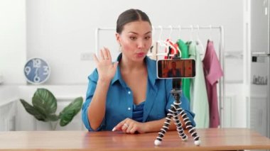 Kadın, oturma odasında tek başına oturan akıllı telefonu kullanarak video bloğu kaydediyor. Tripod kadın filmine cihaz yerleştiriyor. Yeni vlog çevrimiçi canlı yayın yapıyor.