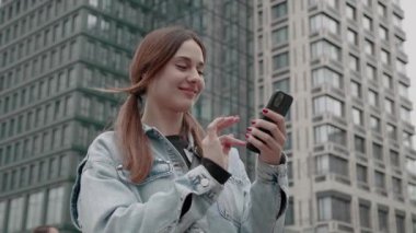 Akıllı telefonlu gülümseyen genç bir kadın kameraya bakıyor ve 
