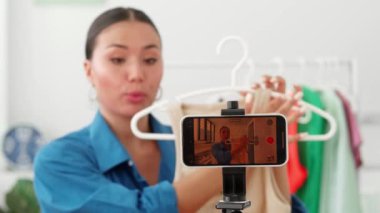 Kadın moda tasarımcısı, başarılı terzi girişimci akıllı telefondan bir vlog kaydediyor, yeni kıyafet koleksiyonunu gösteriyor