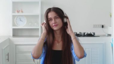 Evdeki mutfakta kablosuz kulaklıkla müzik dinlerken uzun saçlı güzel bir kadın dans ediyor.