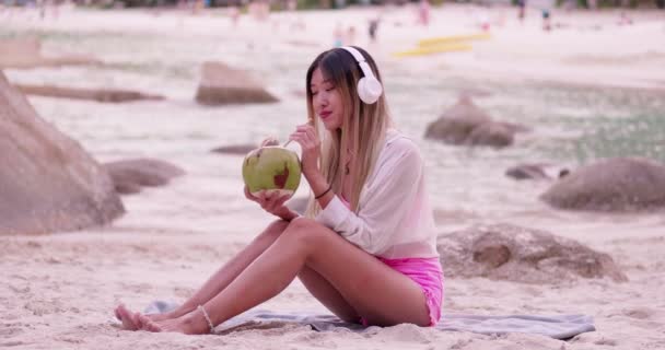 아시아 헤드폰으로 음악을 모래사장의 빨대에서 칵테일을 마신다 — 비디오