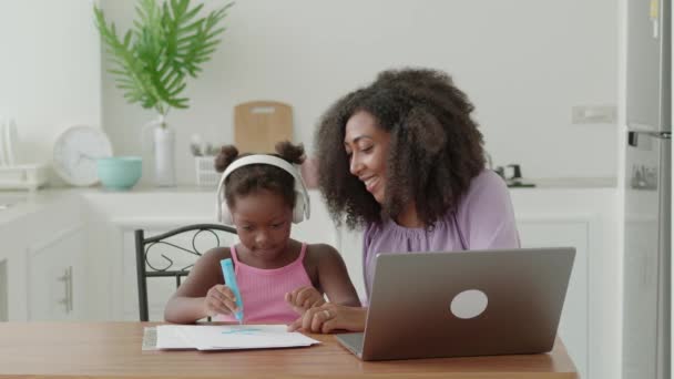 ヘッドフォンの女の子は自宅で彼女のお母さんとノートパソコン上の教育オーディオ描画レッスンを聞いて ホームスクーリング — ストック動画