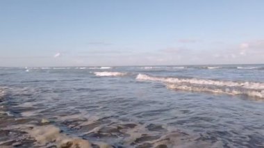 Alçak açı geniş ağır çekim dalgaları sonbahar ışığı altında bir sahilde yuvarlanıyor.