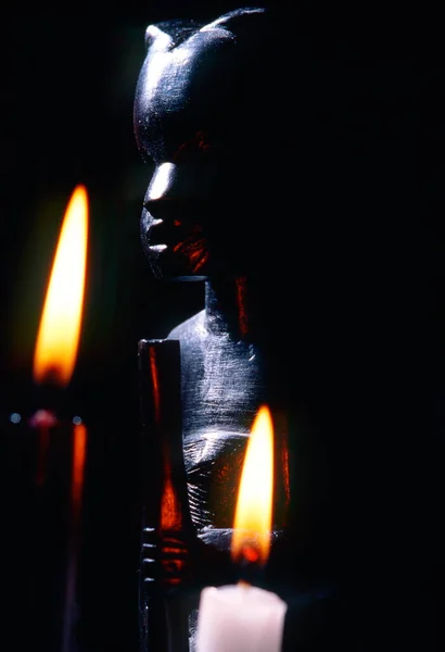 黒と白の2本の燃えているキャンドルを持つアフリカの像の暗いクローズアップ — ストック写真