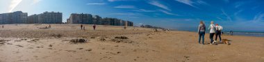 Kumsaldaki panoramik manzara güneşli bir ilkbaharda insanların yürüdüğü ya da plajda oynadığı