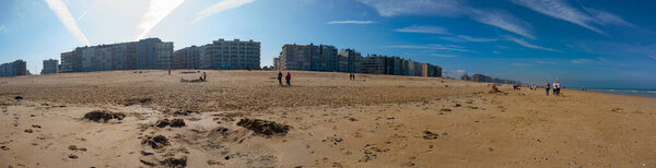 panoramic view on sand beach with people walking or playing on the beach on a sunny springday