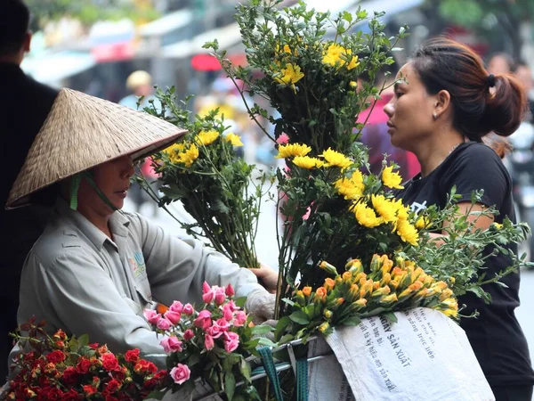 Hanoi, Vietnam. 8 Ağustos 2018. Yerli bir kadın, koni şapkalı, bisikletli bir bayandan çiçek topluyor..