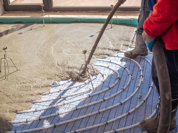 Underfloor heating and energy saving construction. Worker pouring indoor concrete screed with hose.