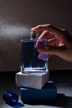 Bir adamın eli mavi bir şişeden parfüm sıkar.