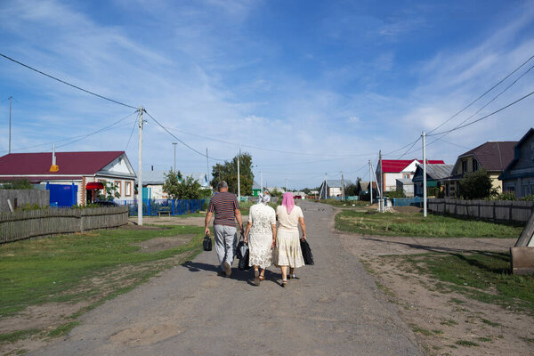 people walk along the road in the village against a beautiful sky