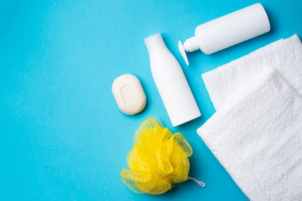 Beyaz havlular, beyaz şampuanlar, sabun, mavi arka planda sarı bez.