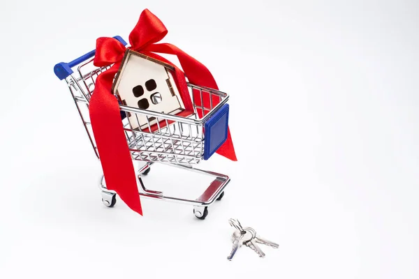 Beyaz arka planda kırmızı kurdeleli bir ev şeklinde bir hediye.