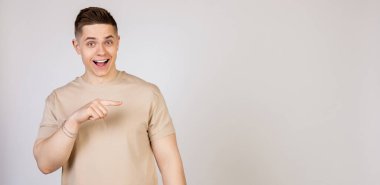 Adam yan tarafı gösteriyor ve gülümsüyor. Genç, çekici, yakışıklı, modern serbest çalışan, girişimci, kameraya bakan işveren öğrencinin fotoğrafı, işaret parmağıyla mekanı kopyalamak için işaret ediyor