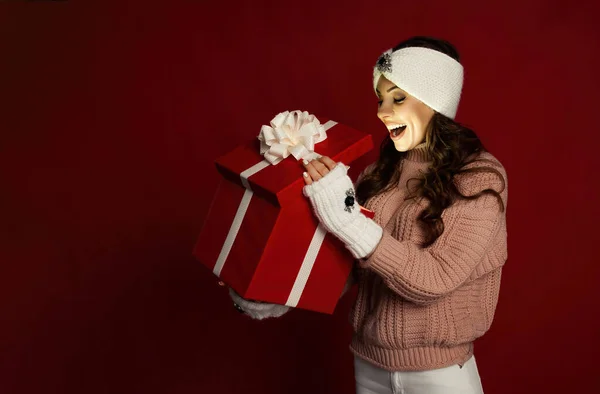 Happy young woman with a present, opening a Christmas present box. Portrait of happy smiling girl opening gift box isolated on red background. — Fotografia de Stock