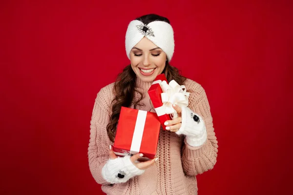 Happy young woman with a present, opening a Christmas present box. Portrait of happy smiling girl opening gift box isolated on red background. — Foto Stock