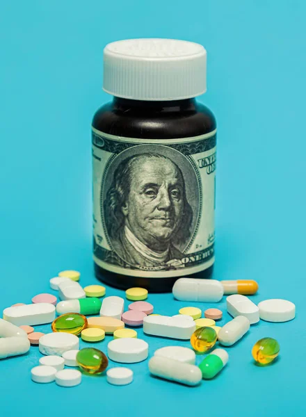 Dinero y pastillas de diferentes colores sobre un fondo azul. El aumento en el costo de la atención médica. El concepto de medicina de seguros, seguros, alto costo, alto costo de medicamentos. — Foto de Stock