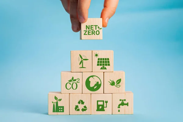 Netto nul en koolstofneutraal concept. Netto nul broeikasgasemissiereductiedoelstelling. Klimaatneutrale langetermijnstrategie. Hand zet houten kubussen met groene netto nul pictogram en groene pictogram op grijze achtergrond. — Stockfoto