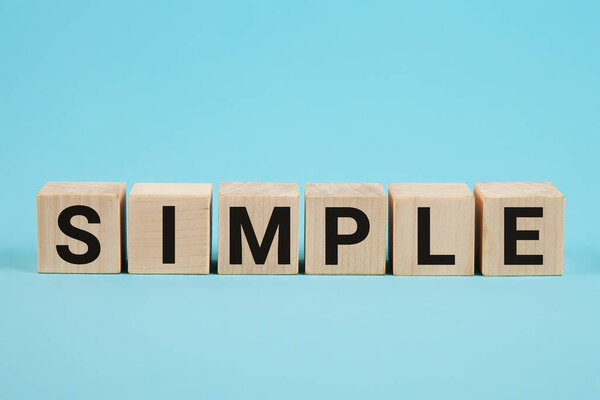 SIMPLE word from wooden blocks with letters, to make something easy, keep it simple concept, blue background.